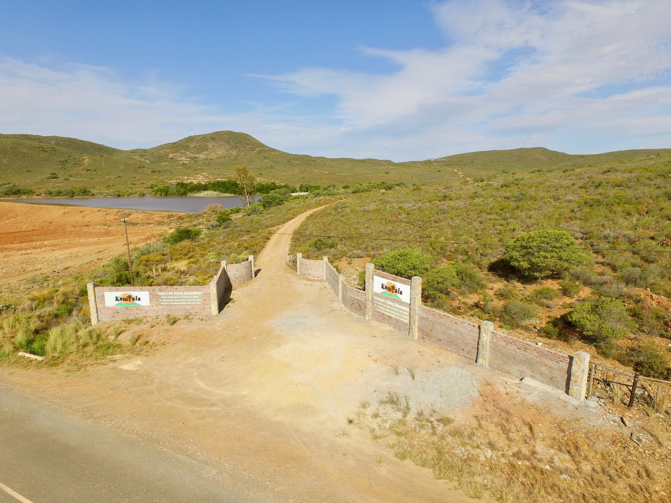 Kampala’s brick entrance and farm road, with the dam and hills beyond
